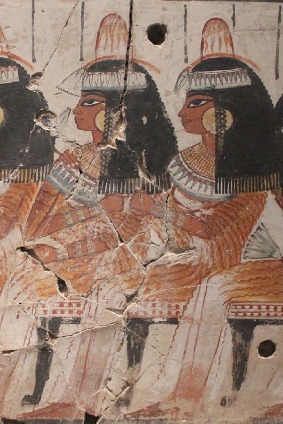 a fragment of an ancient egyptian painting depicting three women seated on chairs. they are wearing long dresses and elaborate headdresses. the artwork is faded and cracked with some paint loss.