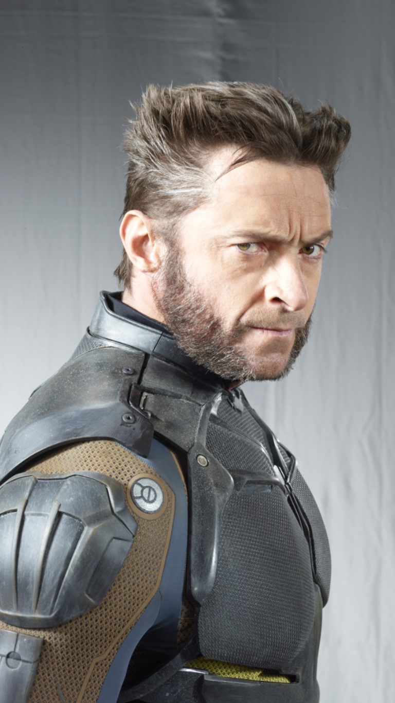 a closeup shot of hugh jackman in his wolverine costume. he has his signature hairstyle and sideburns, and a serious expression on his face. he is wearing a dark armored suit.