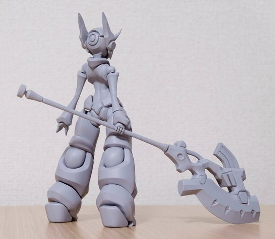 this is a gray model kit of a female robot with large feet, wielding a spearlike weapon. the model is unpainted and unassembled. the robot is standing on a wooden surface. the image is taken from the back and the robot is facing away from the camera.