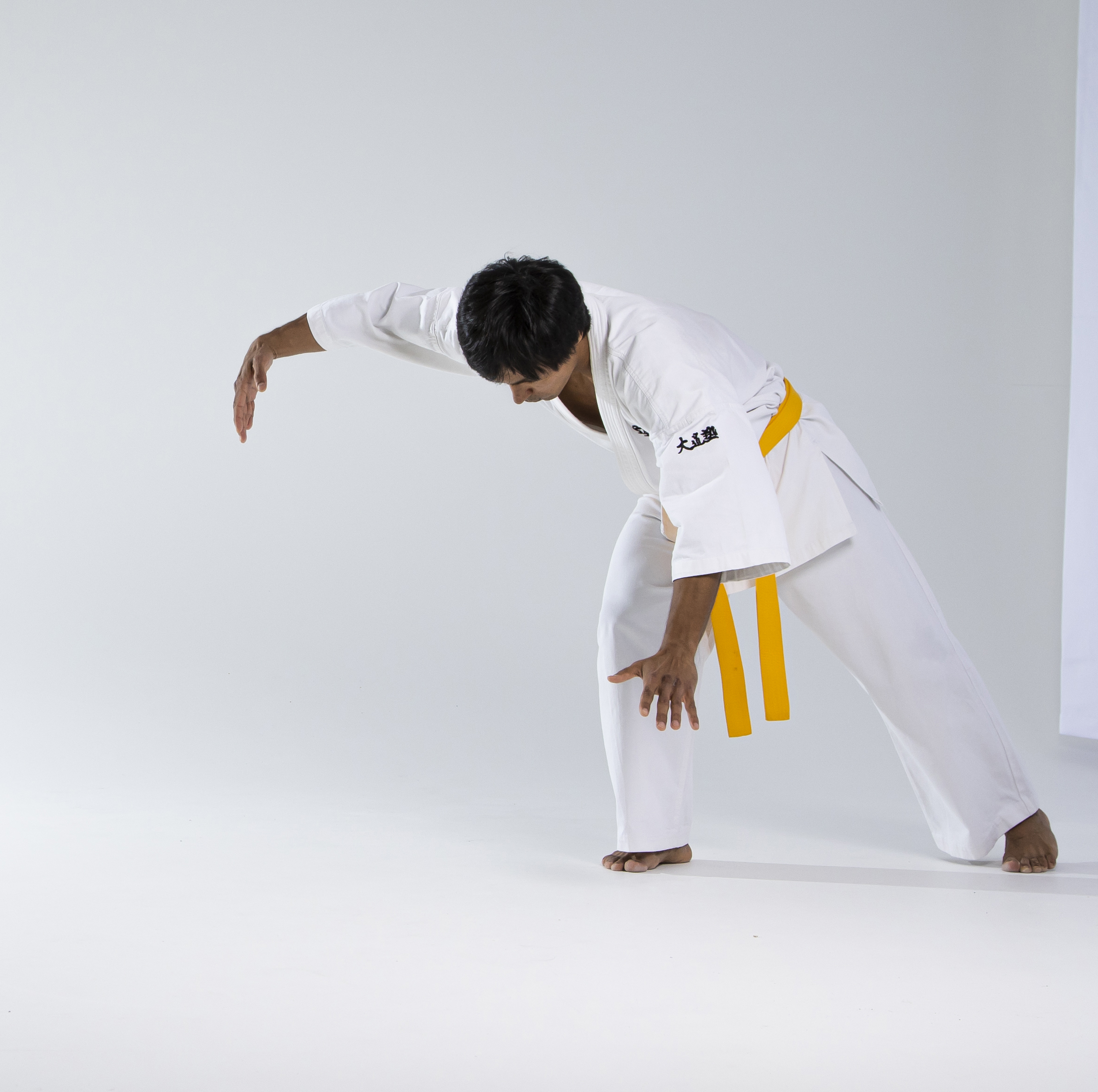 a person in a white karate uniform with a yellow belt is barefoot and leaning forward with arms extended.