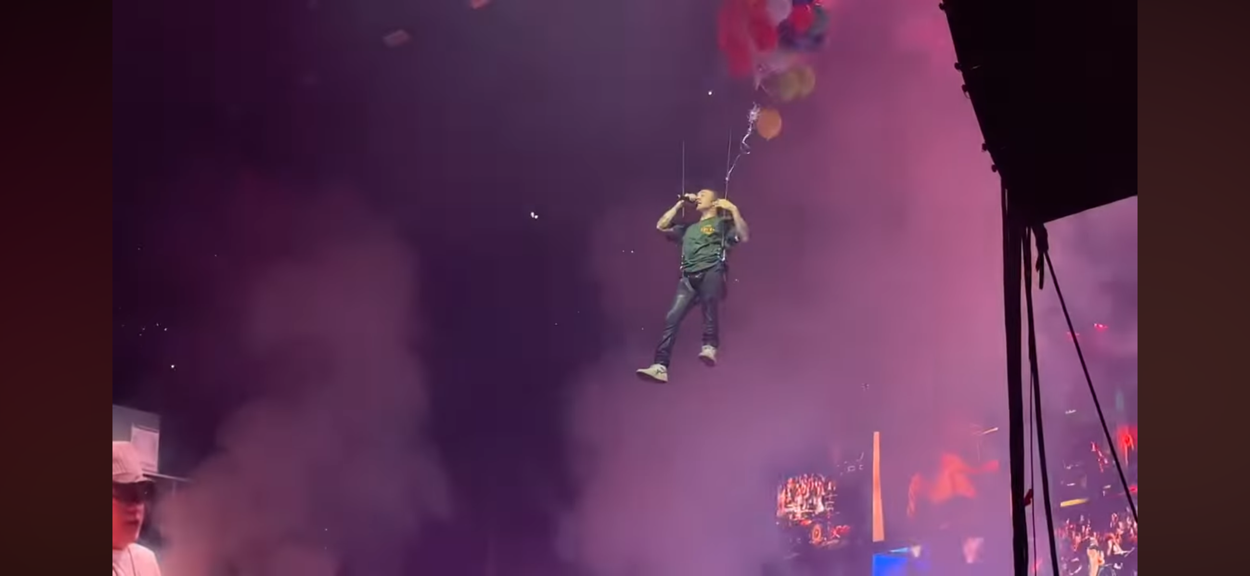 a singer performs at a concert, suspended in the air by wires, with a microphone in hand.  the crowd is cheering and a fog machine is creating a mystical atmosphere. the lights are illuminating the performer, and the stage is filled with smoke.  the singer seems to be enjoying the moment as they sing and interact with the crowd.