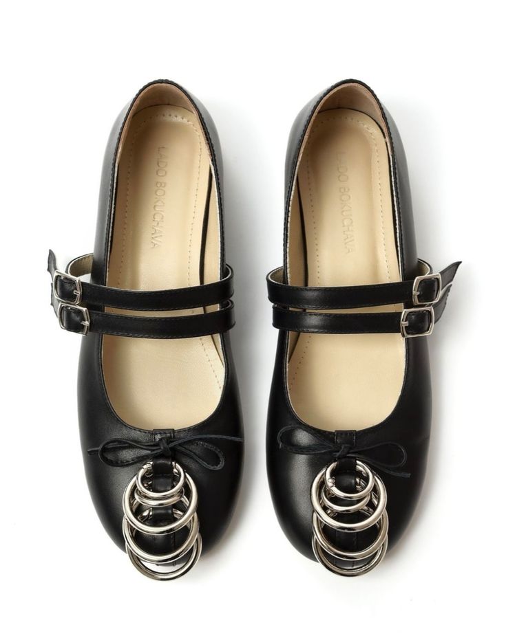 a studio shot shows a pair of black leather women's mary jane shoes.  the shoes are positioned on a white background.  they feature a double strap with buckles, and a distinctive metal ring detail at the front of each shoe. the brand name "ludo boulcava" is subtly visible on the inside of each shoe. the shoes appear to be new and unworn.  the image is welllit and showcases the details of the shoes clearly.