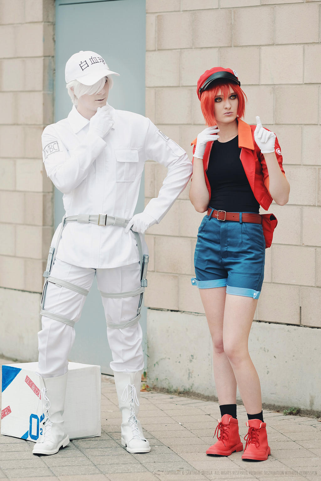 two cosplayers dressed as characters from the anime cells at work! stand next to each other. the cosplayer on the left is dressed as white blood cell, wearing a white cap, uniform, and boots, and has white hair. the cosplayer on the right is dressed as red blood cell, wearing a red cap, jacket, and boots, a black shirt, and blue shorts, and has red hair. they are standing in front of a brick wall and a door.