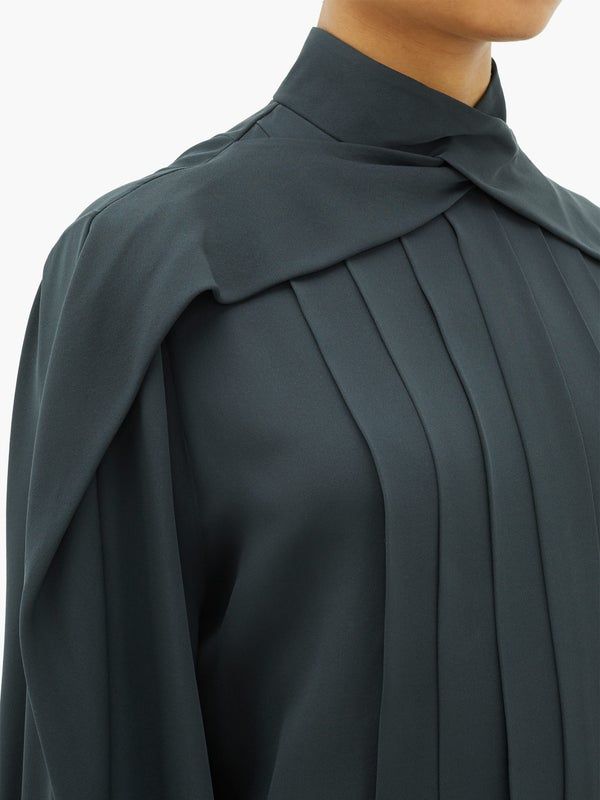 loseup view of a woman's dark green, longsleeved shirt. the shirt features a high neck with a knotted or draped collar, and the bodice is elegantly pleated. the fabric appears to be a smooth, possibly silklike material. the image focuses on the texture and design details of the shirt's collar and pleating.  the overall style is formal and sophisticated.