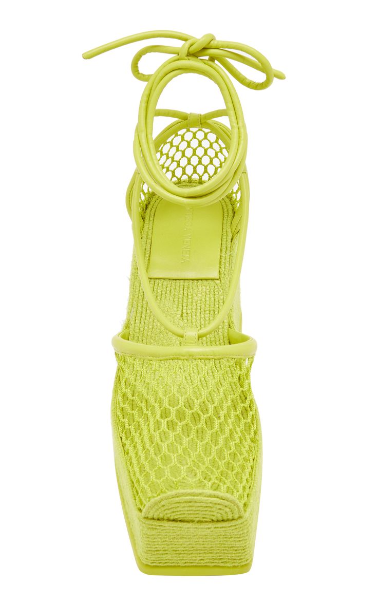 a pair of lime green platform sandals with a mesh upper and laceup closure are shown in the image. the sandals are made of a woven material and have a high platform sole. the sandals are tied up with laces and have a unique design.
