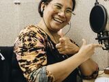 a close up portrait of a happy asian woman in a leopard print blouse holding up her thumbs while recording in a studio.