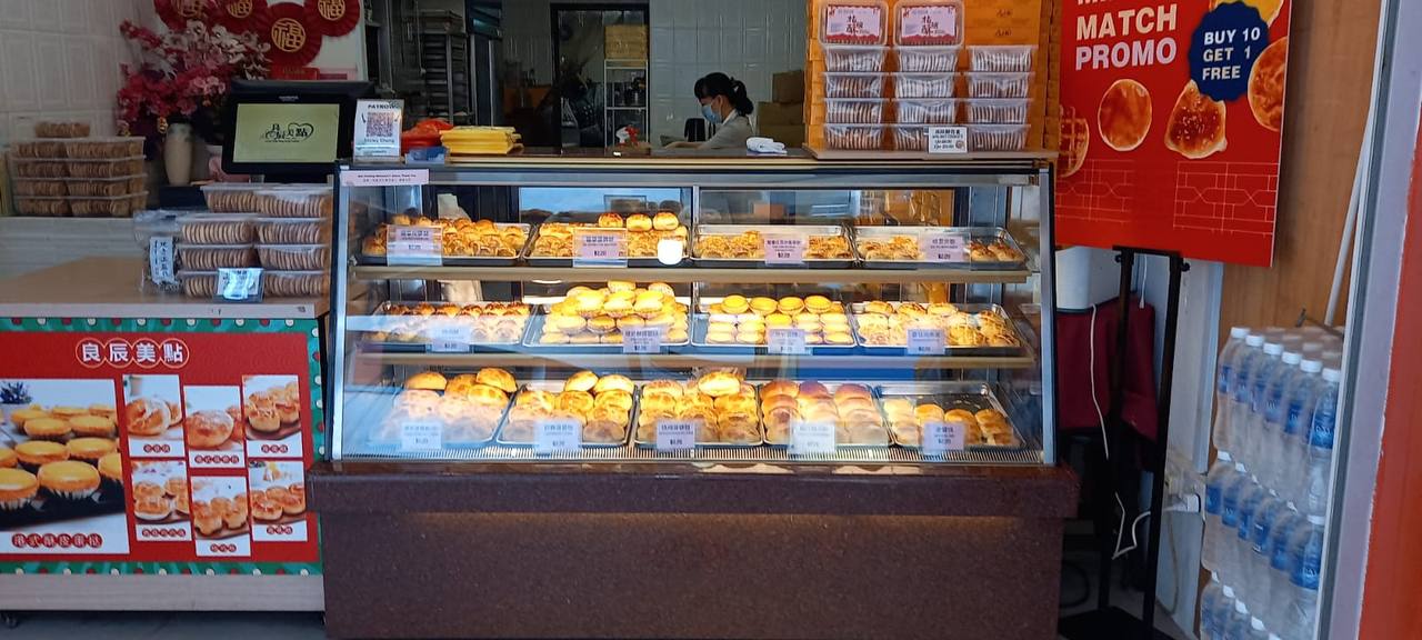 a bakery display case filled with rows of fresh pastries, showcasing various flavors and shapes.  the case is illuminated, highlighting the goldenbrown crusts and inviting customers to indulge in the sweet treats.  a sign advertising a "buy ten get one free" promo for match pastries catches the eye, while a rack of water bottles hints at the option for refreshing beverages alongside the baked goods. the image captures the bustling atmosphere of a bakery, with both the pastries and the signage drawing attention.