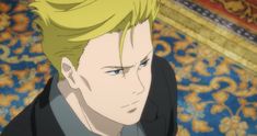 a young man with spiky blond hair and blue eyes looks down and to the side. the lighting is soft and highlights the right side of his face. he is wearing a black collared shirt and a black jacket. he has a serious expression. in the background there's an intricate gold and blue pattern.  it appears to be a screenshot from an anime.