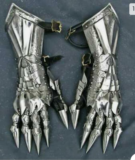 a pair of ornate, metal gauntlets lay spread out on a gray surface.  the gauntlets have hinged finger pieces that extend past the fingertips and end in sharp points.  each section appears separate and designed for flexibility. the metal has a brushed finish.