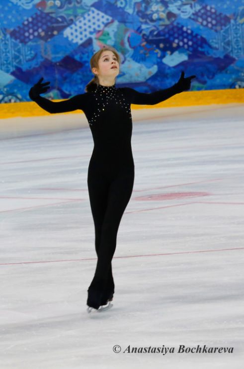 a female figure skater wearing a black suit skates on the ice in an elegant and graceful pose.