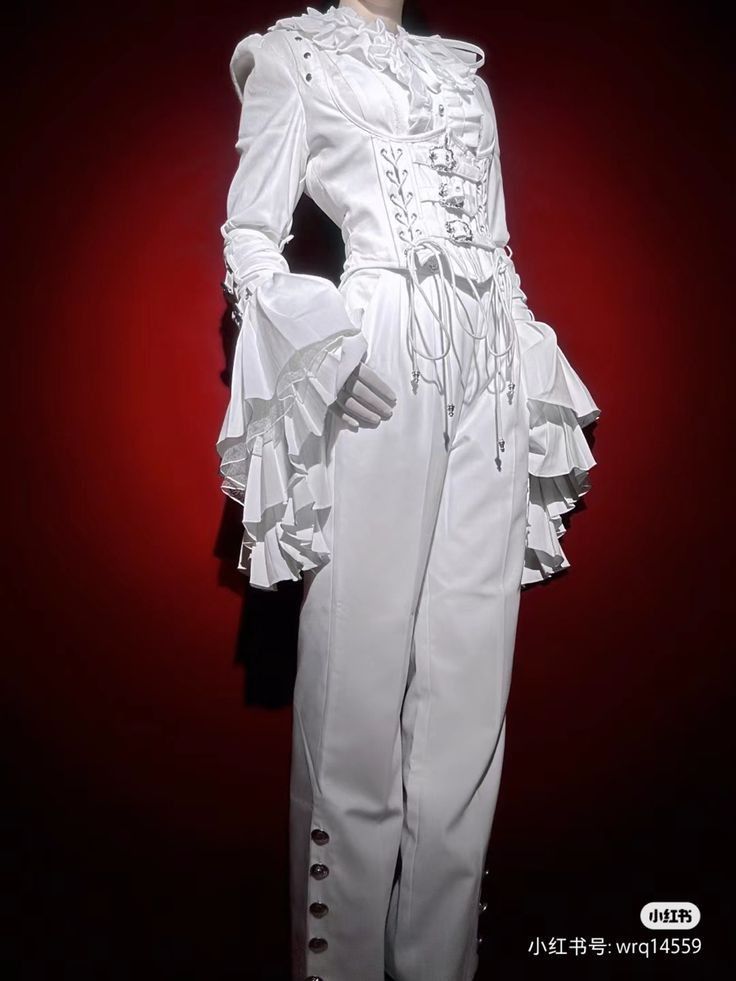 a white outfit is displayed on a mannequin against a red background. the outfit features a ruffled collar, ruffled sleeves, a corsetstyle top, and pants with buttons down the side. the overall style is theatrical and elaborate.