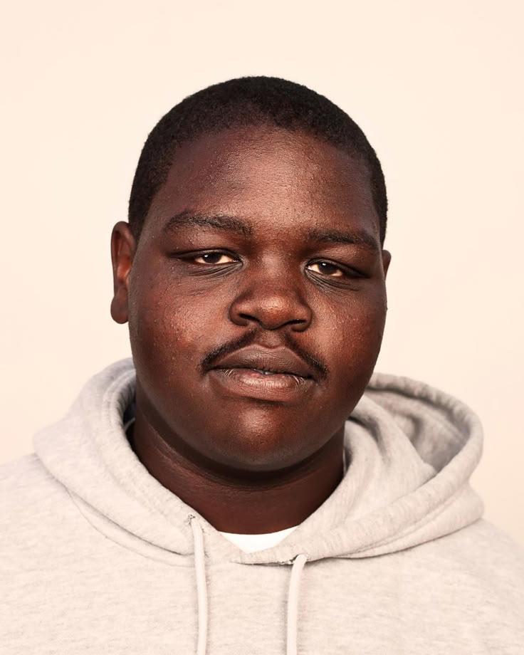 a portrait of a darkskinned man wearing a gray hoodie. he has a mustache and short hair. the background is a neutral color. the photo captures his face, head, and shoulders.