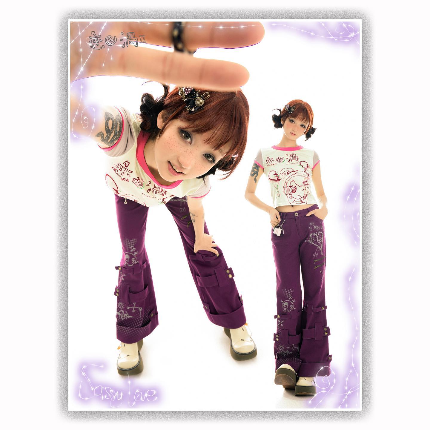 two young women are showcasing a purple pants and cartoon tshirt outfit. the first model is shown in a dynamic pose, hand reaching upwards. the second model is standing in a relaxed pose. both models sport the same attire but vary in their pose and positioning. the background is pristine white, enhancing the focus on the clothing and models. the image reflects a playful and fashionable aesthetic consistent with japanese street style.