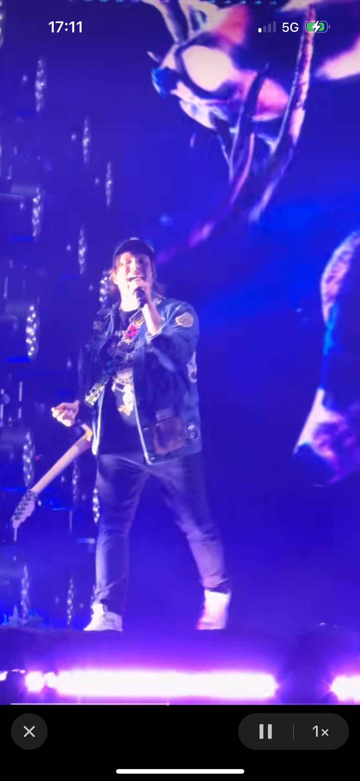 a singer on stage performs in front of a crowd. he's playing a guitar, singing into a microphone, with purple lighting on stage. the crowd is out of focus in the background.