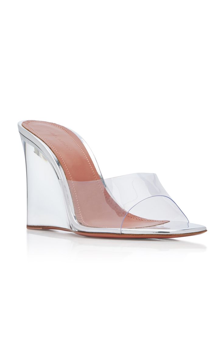 pair of women's silver metallic and clear pvc wedge mules are showcased against a white background. the shoes have a transparent wedge heel and a clear pvc strap across the toes. the insole is a light brown color. the shoes are angled slightly to the left, presenting a side view.  they appear to be new and unused.