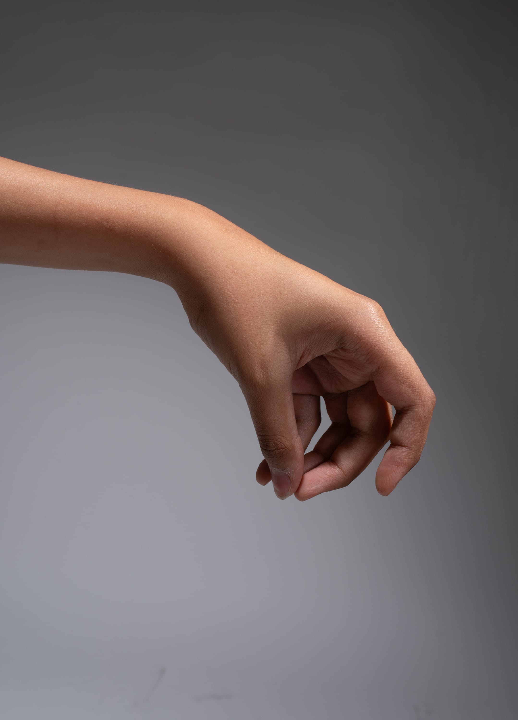 an image of a right arm and hand extended downwards against a light gray background. the image is lit with studio lighting.