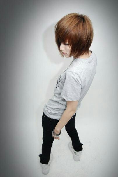 a young woman with a stylish short brown hairstyle is captured in a studio setting. she's wearing a gray tshirt, black skinny jeans, and white sneakers. she's striking a pose with her head tilted down and her arms relaxed at her sides, showcasing her trendy and fashionable look. the image is shot from a high angle, creating a dynamic perspective.