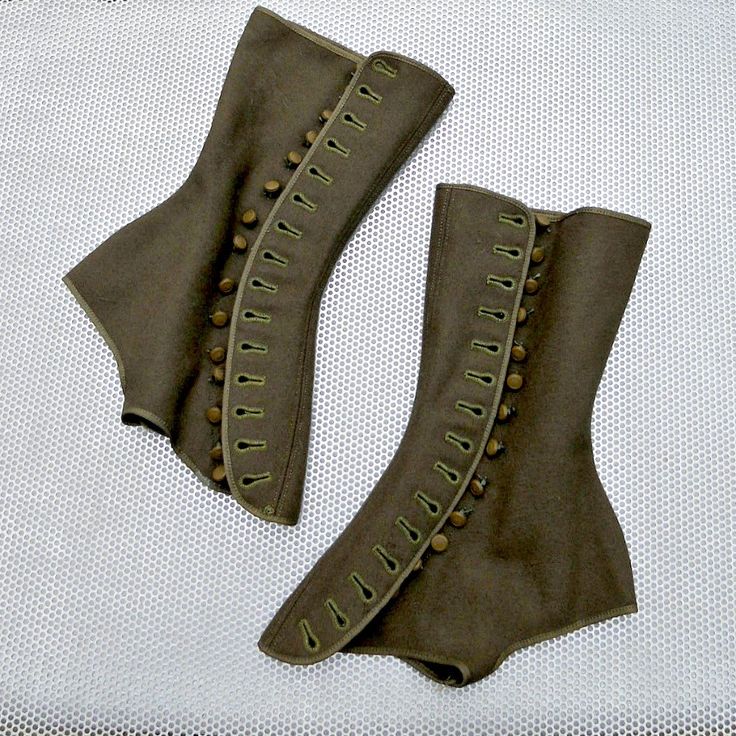 a pair of brown wool kneehigh boots with button and loop detailing. they are vintage style boots. one boot has a large flap that covers the bottom part of the boot, while the other boot is closed up. both boots have a button and loop closure that goes all the way up the leg.  the boots are sitting on a white surface with a grid pattern.