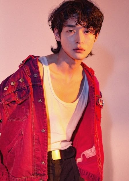 a portrait of an asian man with a mullet hairstyle, wearing a red denim jacket with studs on the shoulders, a white tank top, and black pants with a gold belt buckle. he is posing in a studio with a soft, diffused light.