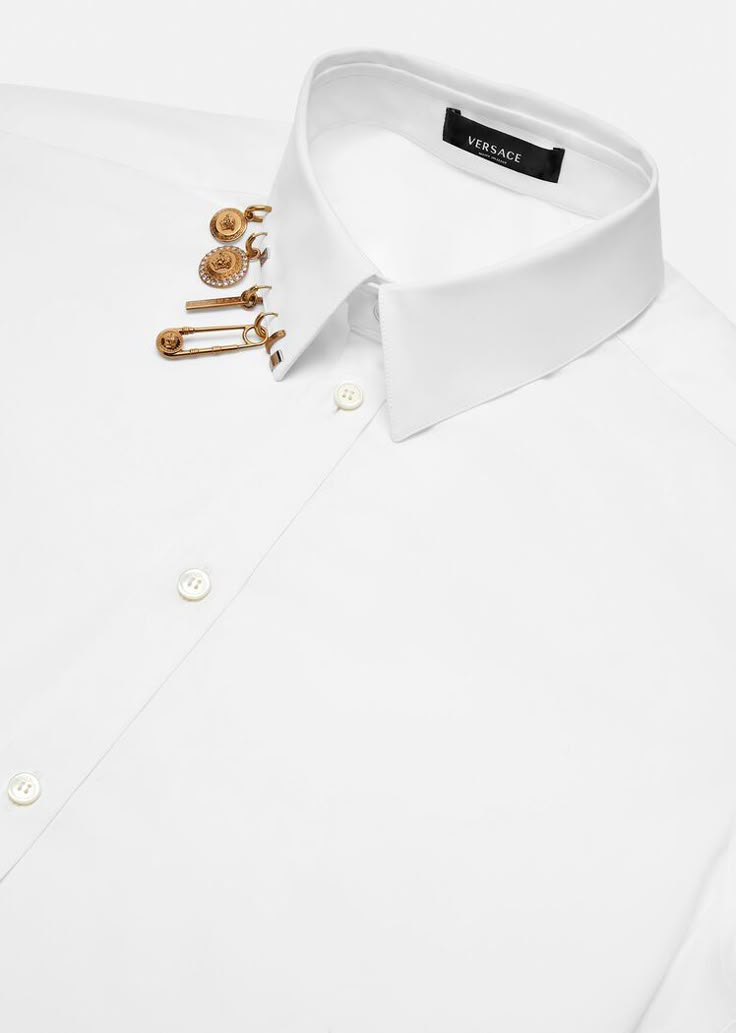 a white collared shirt with gold versace accessories pinned to the collar.