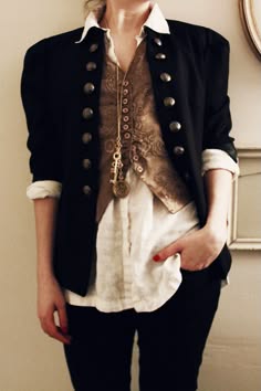 a woman wearing a black jacket, white shirt, and black jeans. she has a gold necklace with a key pendant. her hair is blonde and she is looking down. she is in a casual, trendy, and elegant style.