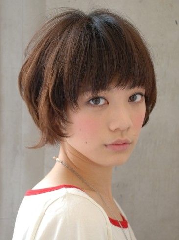 a young woman with short brown hair is looking at the camera. she has her hair styled in a bob with bangs. she is wearing a white shirt with a red collar and a necklace. she has a cute and innocent expression.