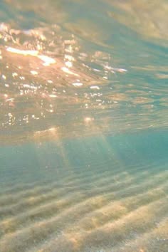a beautiful underwater image of clear blue water with waves, sand and sun shining through the water.