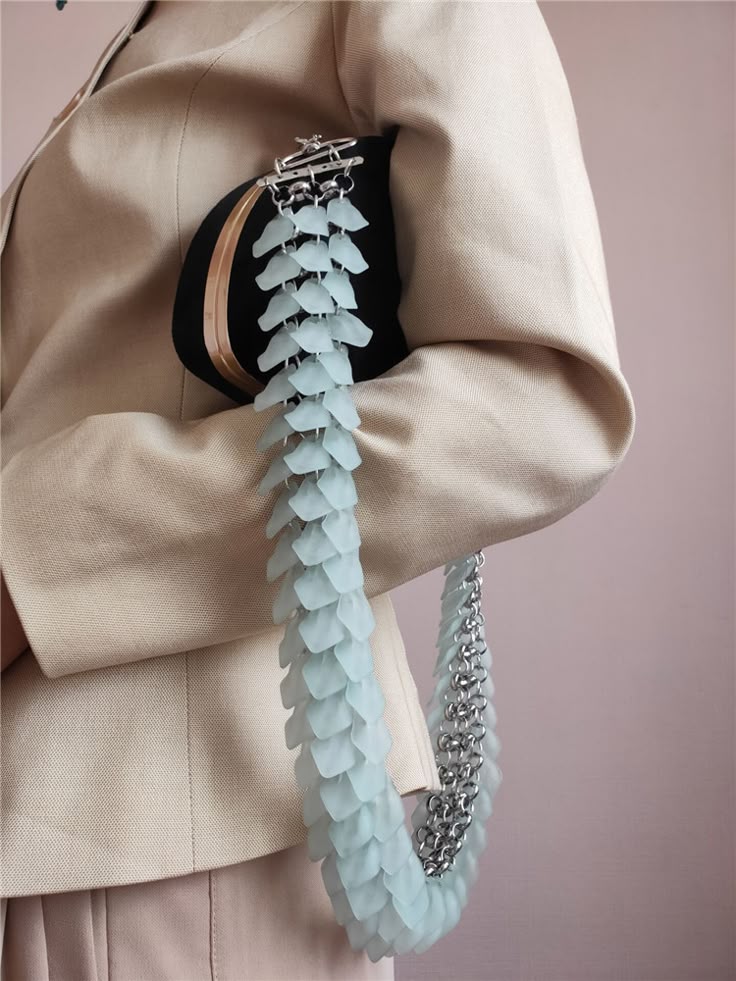 a person is wearing a beige blazer and holding a black purse. the purse has a handle made of light blue scales and a silver chain. the purse is clasped at the top.