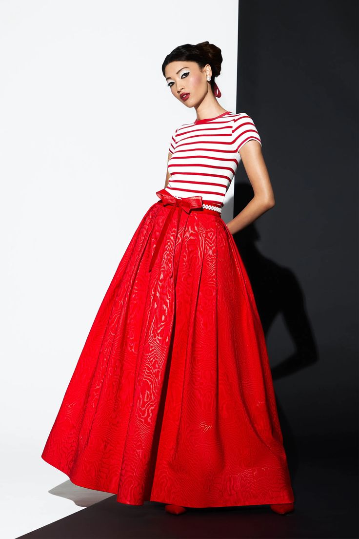 a woman in a red skirt and a striped shirt is posing for a photo shoot. she is standing on a black and white background. her skirt has a red bow around the waist. she is looking at the camera with a serious expression on her face.