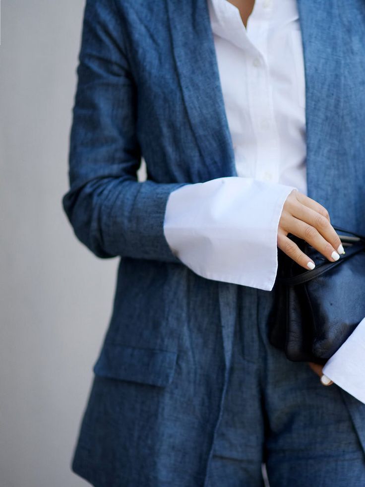 a woman is wearing a blue blazer and matching shorts over a white collared shirt, holding a black bag.