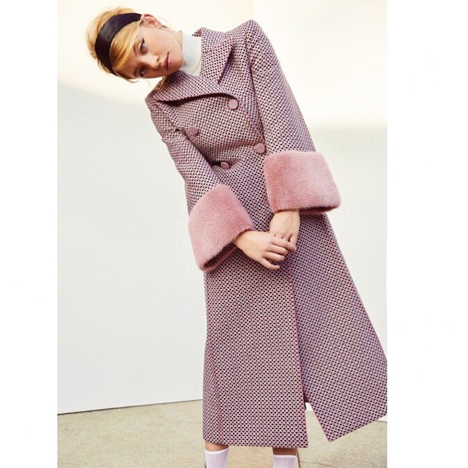 the image showcases a female model wearing a stylish, doublebreasted midi coat. the coat is a light pink with a noticeable textured tweedlike fabric.  the cuffs are trimmed with a light pink fur. the model is wearing a black headband and a white turtleneck underneath, accentuating the coat.  she's posing slightly angled, showcasing the coat's details against a plain white background.  the overall look is elegant and high fashion.