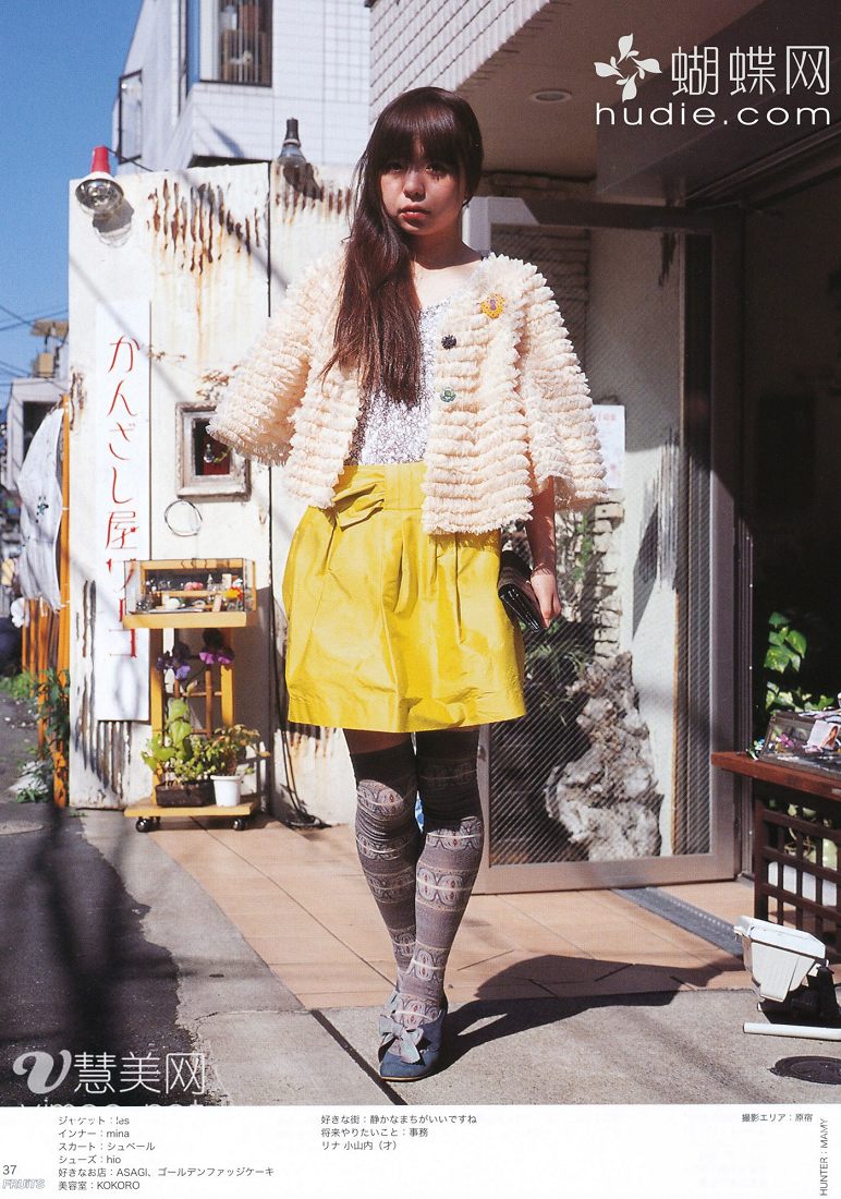 young woman poses for a street style photo in japan. she is wearing a white fuzzy jacket, a sparkly silver top, a yellow skirt, patterned tights, and black shoes with bows. the text on the photo indicates that she likes the stores asagl and golden fudge cake, and that she wants to work in an office.