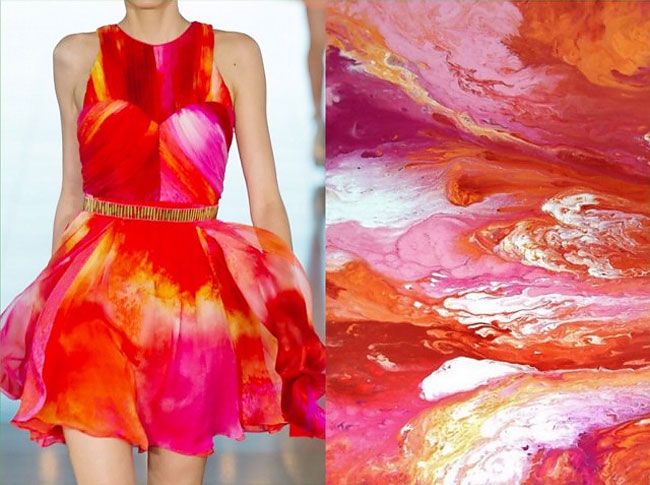 a woman is wearing a pink and orange dress that has an abstract paint design. the right side of the image shows the abstract paint design that is on the dress. it is a very colorful and vibrant design. the woman is standing with her arms at her side and is looking at the camera. the background is a light blue.