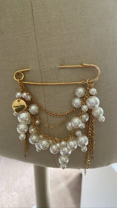 a closeup of a beautiful gold brooch adorned with multiple strands of pearls and gold chains. the brooch is pinned to a creamcolored fabric background. the pearls are large and lustrous, adding a touch of elegance and sparkle to the piece. the gold chains and clasp complement the pearls perfectly. this brooch is a perfect accessory for a special occasion, like a wedding or bridal shower.