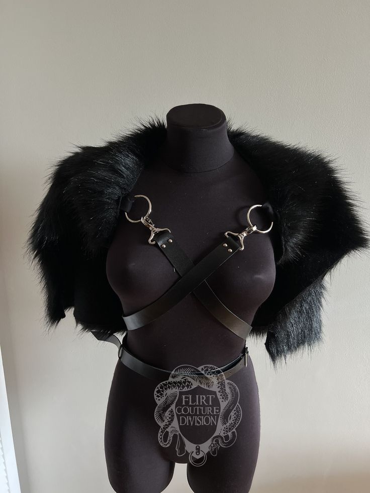 a black faux fur shrug with black leather harness and belt. the harness has two rings in front and the belt has a buckle on the back. the shrug is made of soft fur and the harness is made of smooth leather.