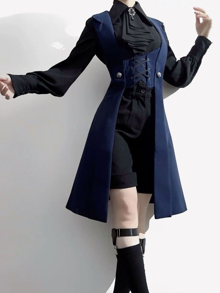 a person is shown from the knee up, modeling a navy blue, long waistcoat with a corsetstyle closure in the front over a white buttonup shirt with a ruffled collar and black highwaisted shorts. the model is also wearing black socks and buckled shoes. they are posing with their arms outstretched and one leg slightly bent.  the background is a simple offwhite wall.