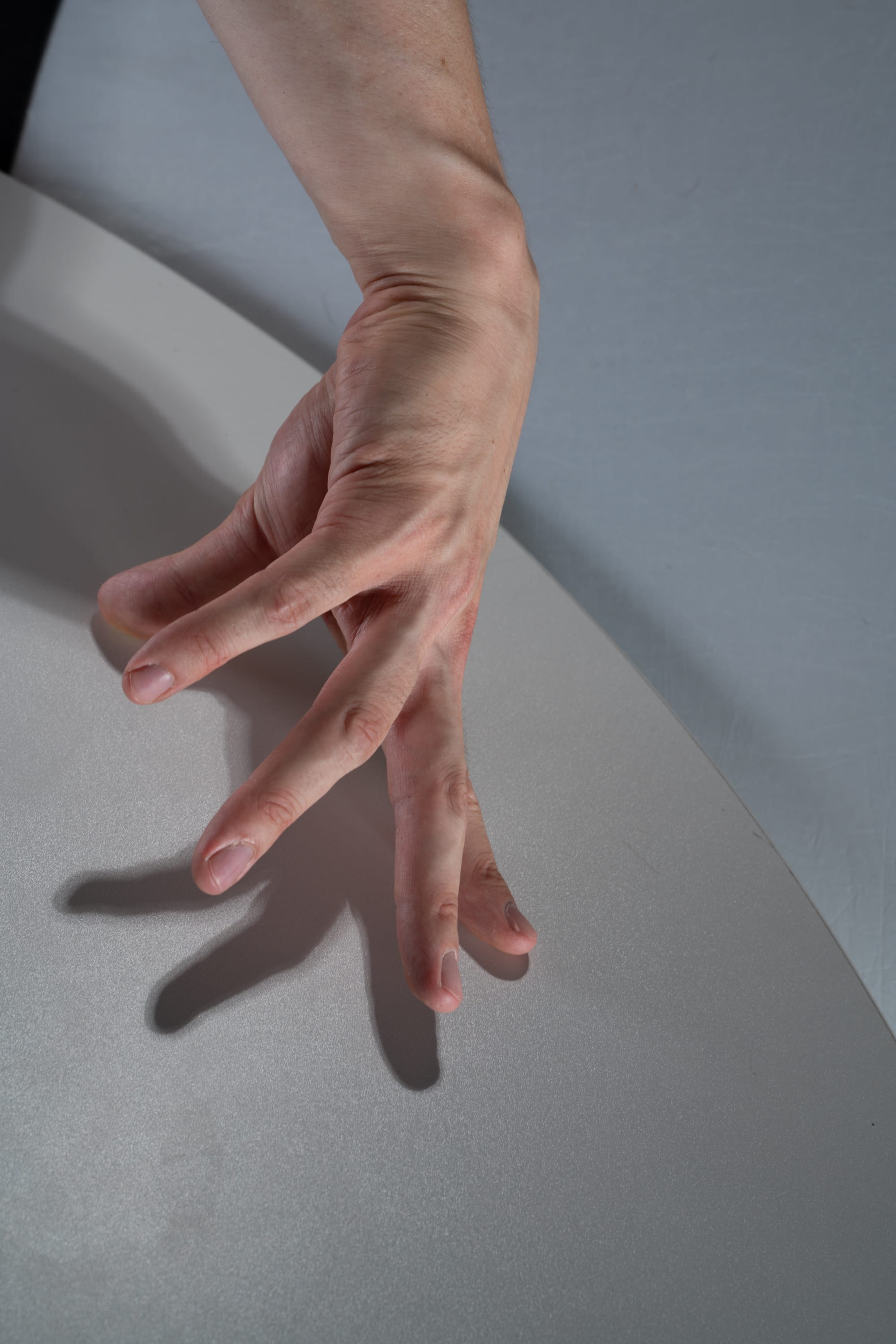 a closeup shot of a hand resting on a white surface. the fingers are slightly splayed, creating a distinct shadow that mirrors the hand's shape. the soft studio lighting emphasizes the texture of the skin and the subtle contours of the hand.