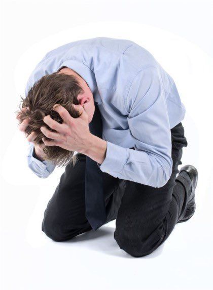 a man dressed in a blue shirt and black trousers is kneeling on the floor with his head in his hands, looking deeply distraught.  his body language and posture convey a sense of extreme sadness,  stress, and hopelessness. he appears to be in emotional distress or experiencing a breakdown.