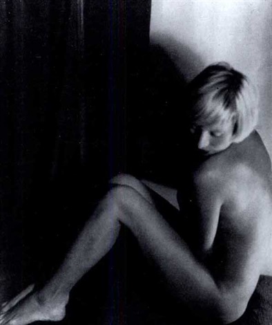 the black and white photograph depicts a young, slender woman sitting hunched over, her body partially obscured by shadow.  she's nude, and her posture suggests introspection or sadness. the lighting is dramatic, with strong contrast between the brightly lit parts of her body and the deep shadows. the background is dark and indistinct, drawing attention to the woman's form.  the overall mood is somber and intimate. the image has a grainy quality, suggestive of film photography.