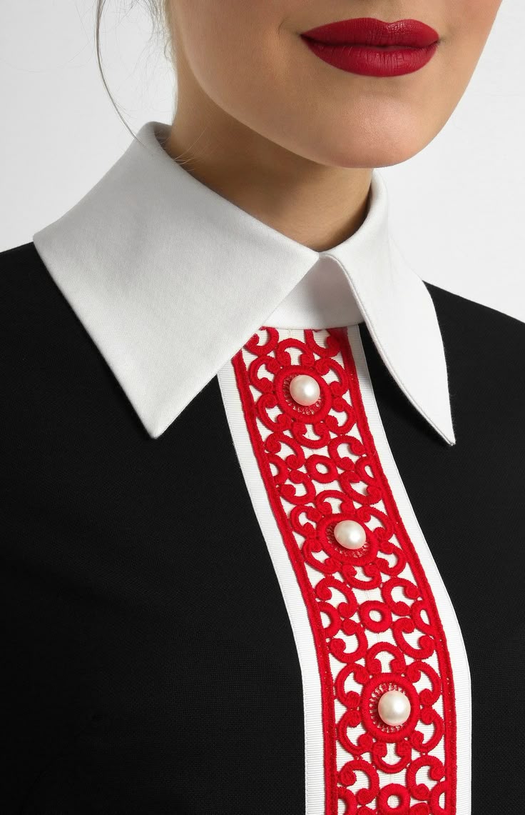 a closeup of a black dress with a white, pointed collar and a vertical stripe of red embroidery adorned with pearls. the model has red lipstick on.