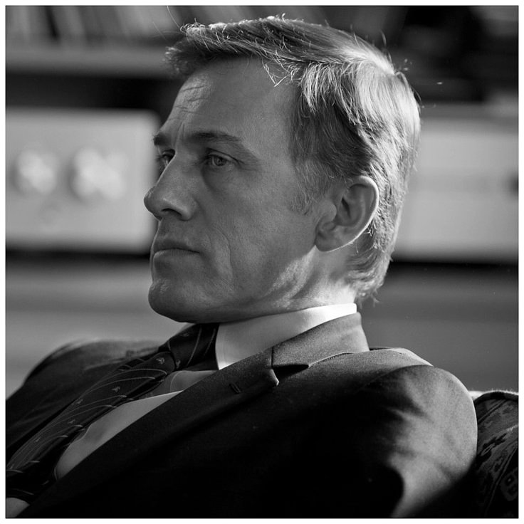 a black and white portrait of a man in a suit and tie, shown in a side profile with a serious expression.