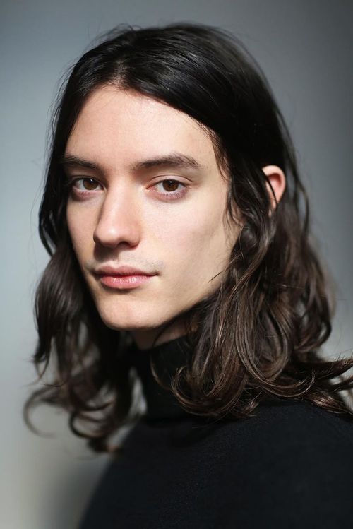 a portrait of a handsome man with long brown hair, wearing a black turtleneck shirt, looking serious.