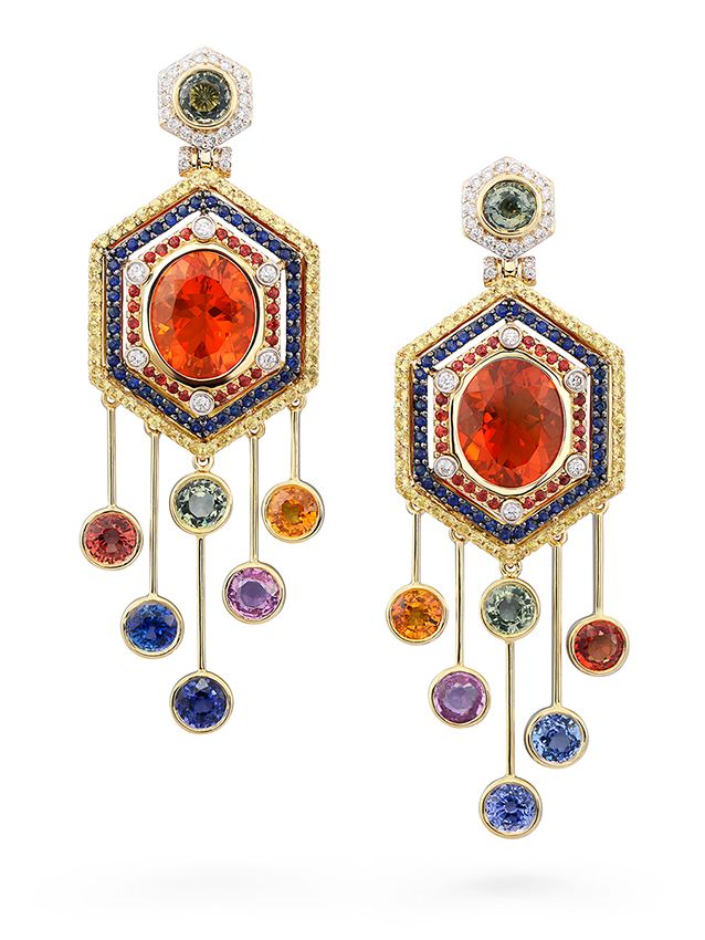 a pair of elegant gold earrings adorned with precious gemstones. the earrings feature a hexagonal design with a large orange gemstone in the center surrounded by smaller sapphire, diamond and yellow gemstones. the hexagonal center hangs from a series of delicate chains with a cluster of vibrant sapphire gemstones in various hues.