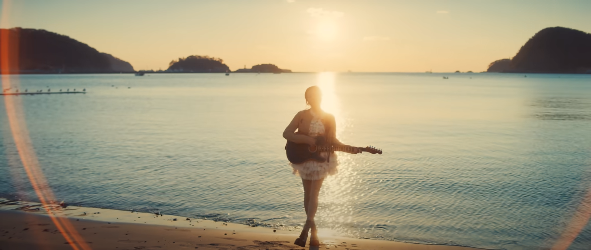 a woman in a white dress stands on a beach at sunset, playing a guitar. the ocean stretches out before her, and the sun is setting behind her, creating a warm, golden glow. the scene is serene and tranquil, evoking a sense of peace and relaxation.