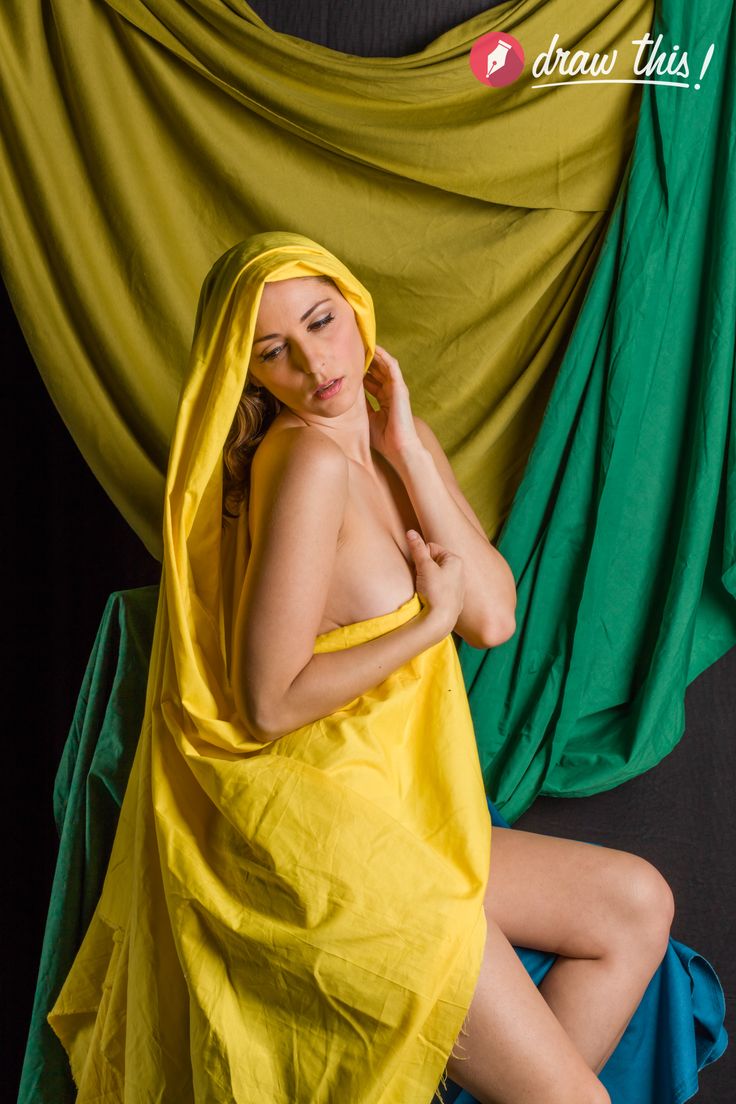 a woman with long brown hair drapes herself in a vibrant yellow fabric against a backdrop of green and yellow fabric.  the lighting is soft, creating a sensual and artistic mood.