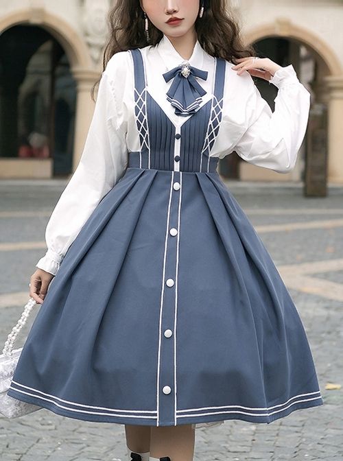 a woman is standing outdoors wearing a blue and white lolita fashion outfit. the outfit features a white blouse with a bow tie, and a blue jumper dress with white trim and buttons down the front. the skirt of the dress is pleated and falls to her knees. she is carrying a small white purse. the image is taken from an eyelevel perspective and the lighting is natural daylight.