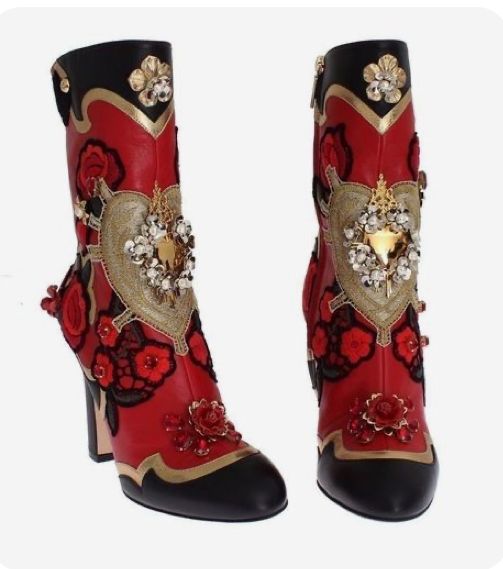 two red and black women's boots are displayed against a white background. the boots are decorated with gold accents, floral details, and a large, jeweled heartshaped embellishment. the highheeled boot on the left is angled slightly, showcasing its side profile, while the boot on the right is positioned frontally. the design is elaborate and ornate.
