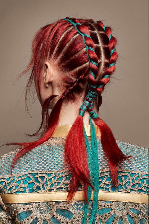 a woman with long, red hair is wearing a blue and gold outfit. her hair is braided with blue ribbon.