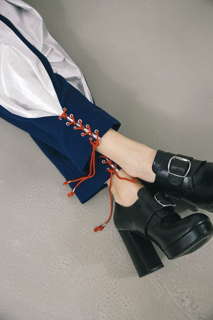 the image shows a person wearing blue pants with red laces and black platform shoes with buckles.