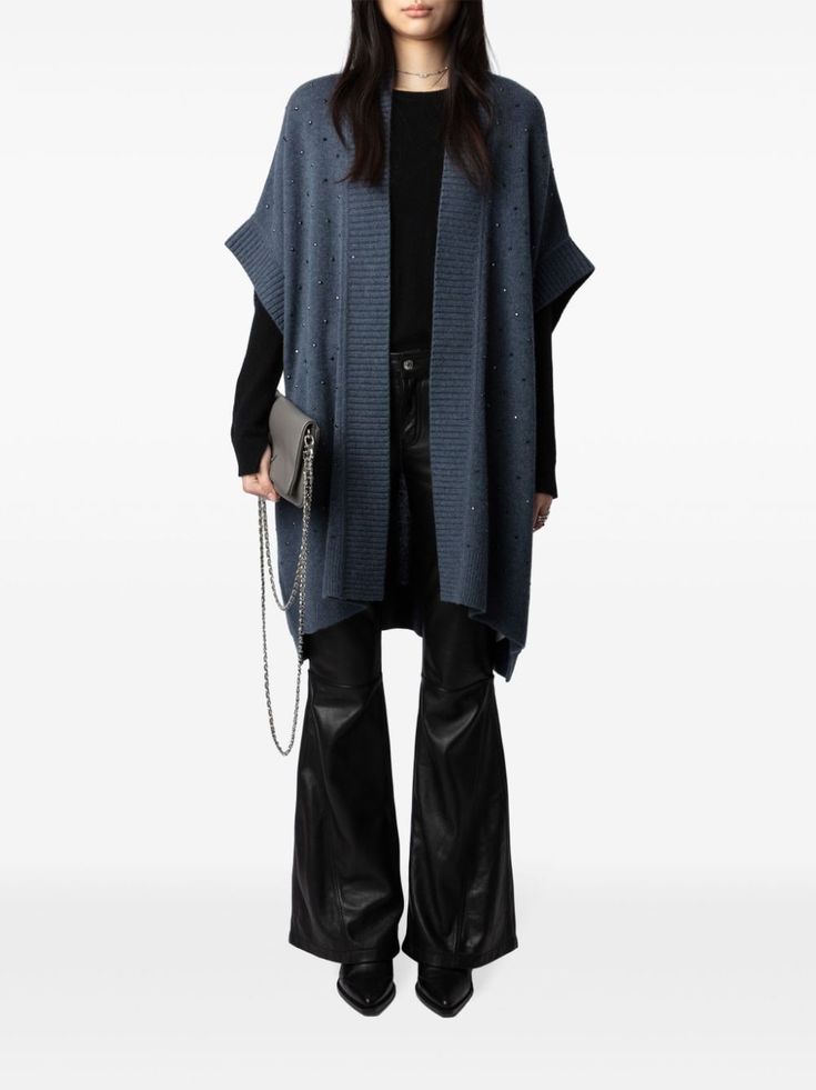 a woman is wearing a blue cardigan with a black top, black leather pants, and black boots. she is holding a grey chain bag in her left hand. she is standing and posing in front of a white background.